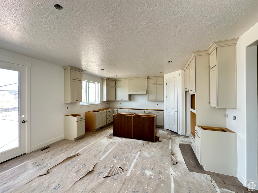 Kitchen with a center island, a textured ceiling, cream cabinetry, and baseboards