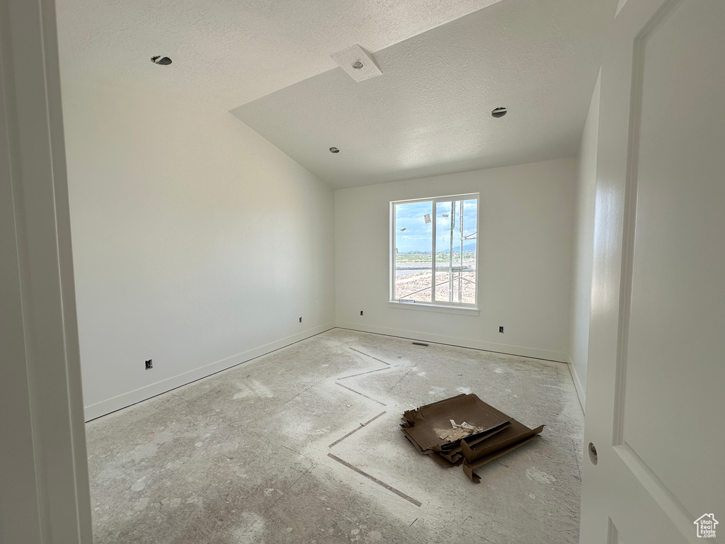 Spare room with a textured ceiling, lofted ceiling, and baseboards