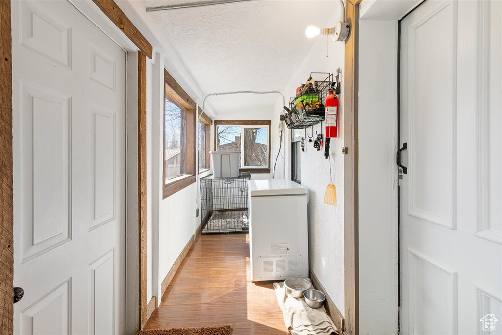 Hallway featuring baseboards, light wood-style floors, and a textured ceiling