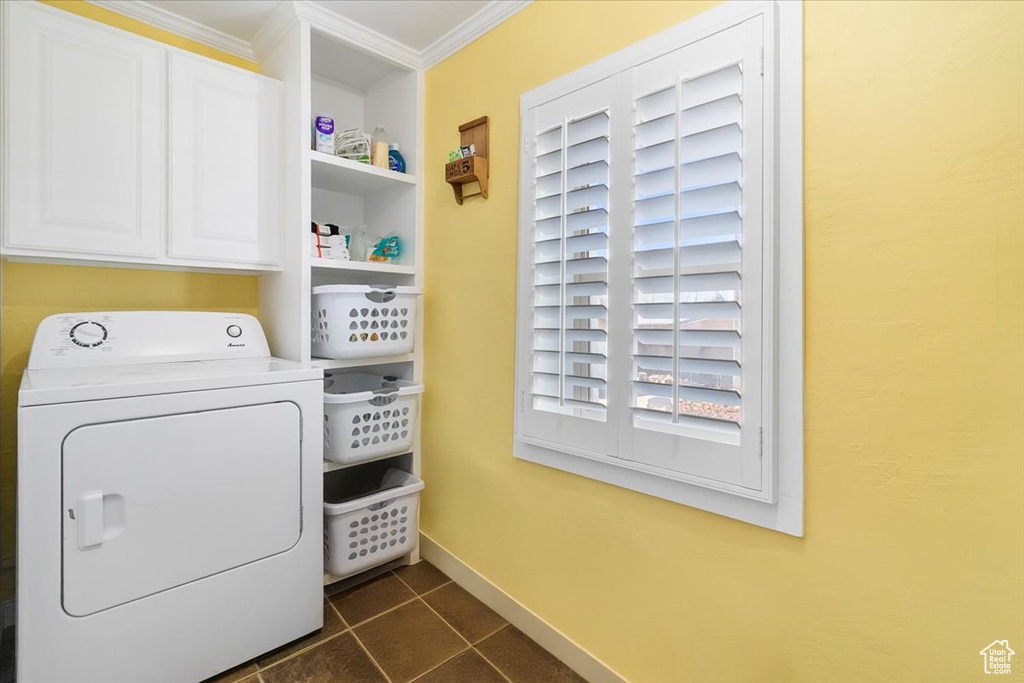 Clothes washing area with crown molding, dark tile patterned floors, baseboards, washer / dryer, and cabinet space