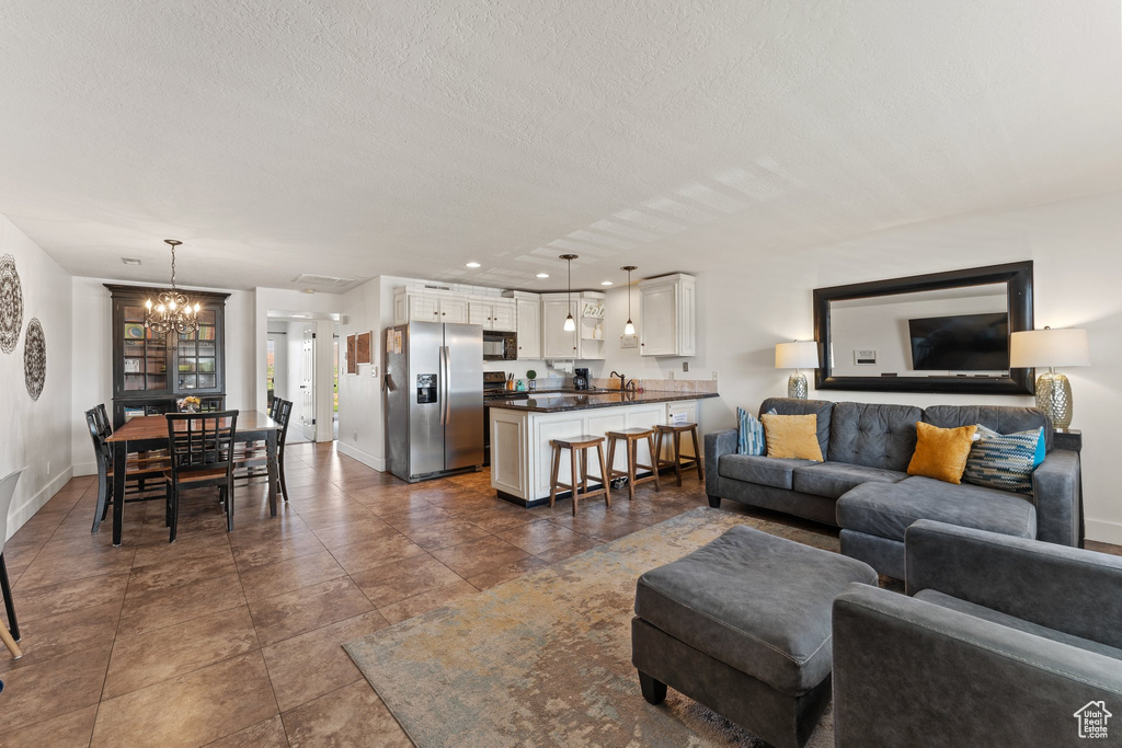 Living room featuring a textured ceiling, a notable chandelier, and baseboards