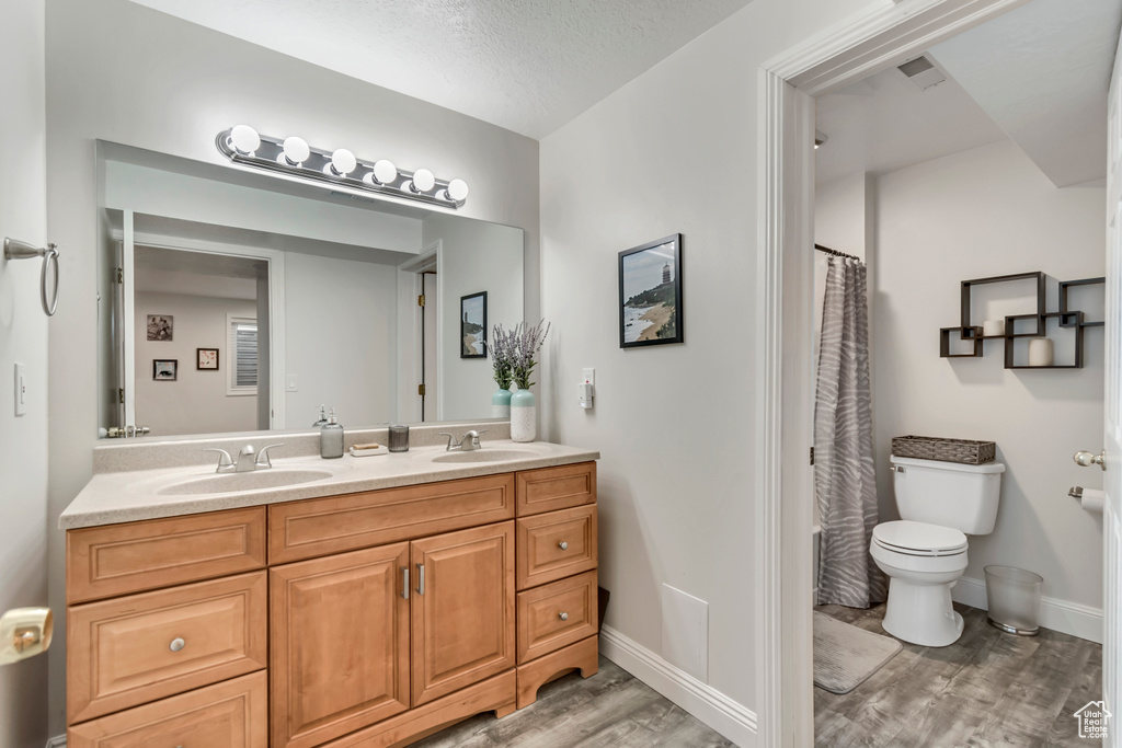 Full bath featuring toilet, a sink, double vanity, and wood finished floors