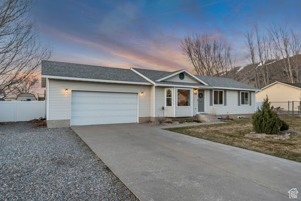 Ranch-style home with driveway, an attached garage, fence, and a shingled roof