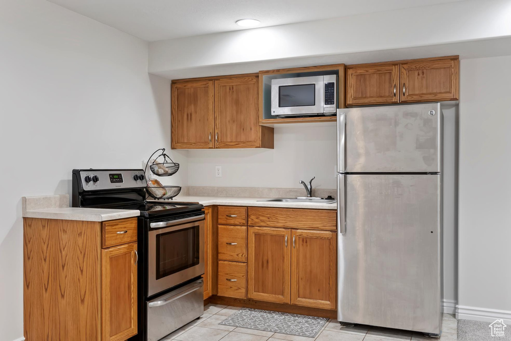 Kitchen with light countertops, a sink, stainless steel appliances, and brown cabinets