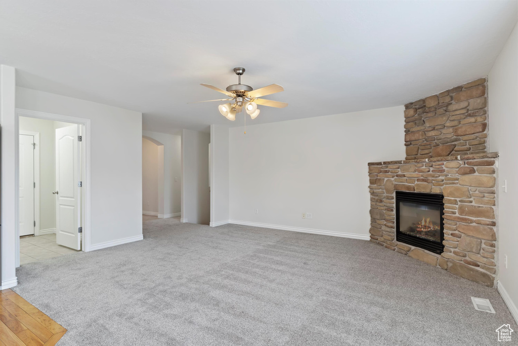 Unfurnished living room with carpet, baseboards, arched walkways, a ceiling fan, and a fireplace