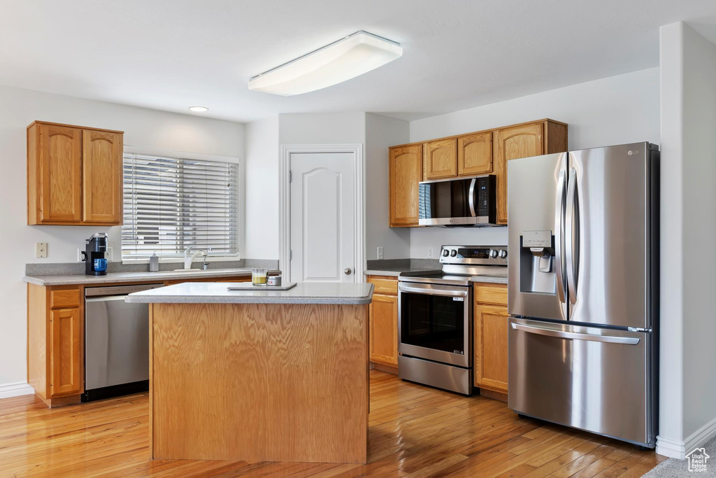 Kitchen featuring light countertops, light wood-style flooring, stainless steel appliances, a sink, and a center island