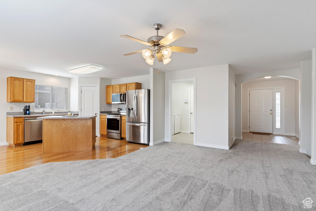 Kitchen with stainless steel appliances, arched walkways, ceiling fan, and light carpet