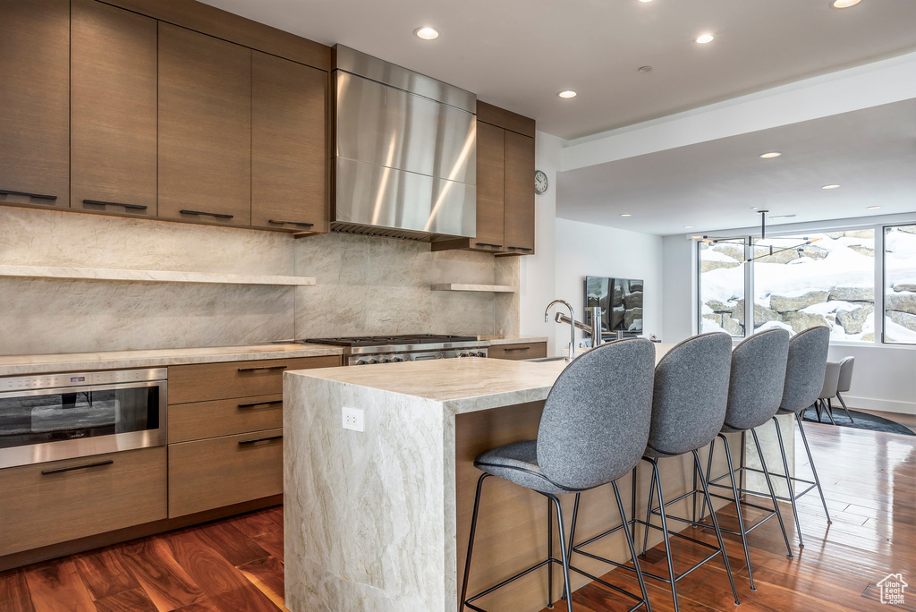 Kitchen with modern cabinets, wall chimney range hood, decorative backsplash, recessed lighting, and a kitchen bar