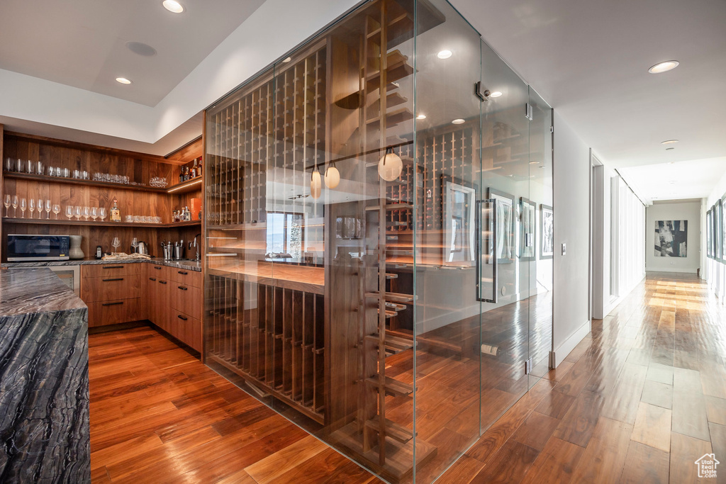 Bar with black microwave, wood finished floors, and recessed lighting