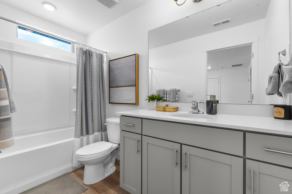 Bathroom with toilet, vanity, shower / bathtub combination with curtain, wood finished floors, and visible vents