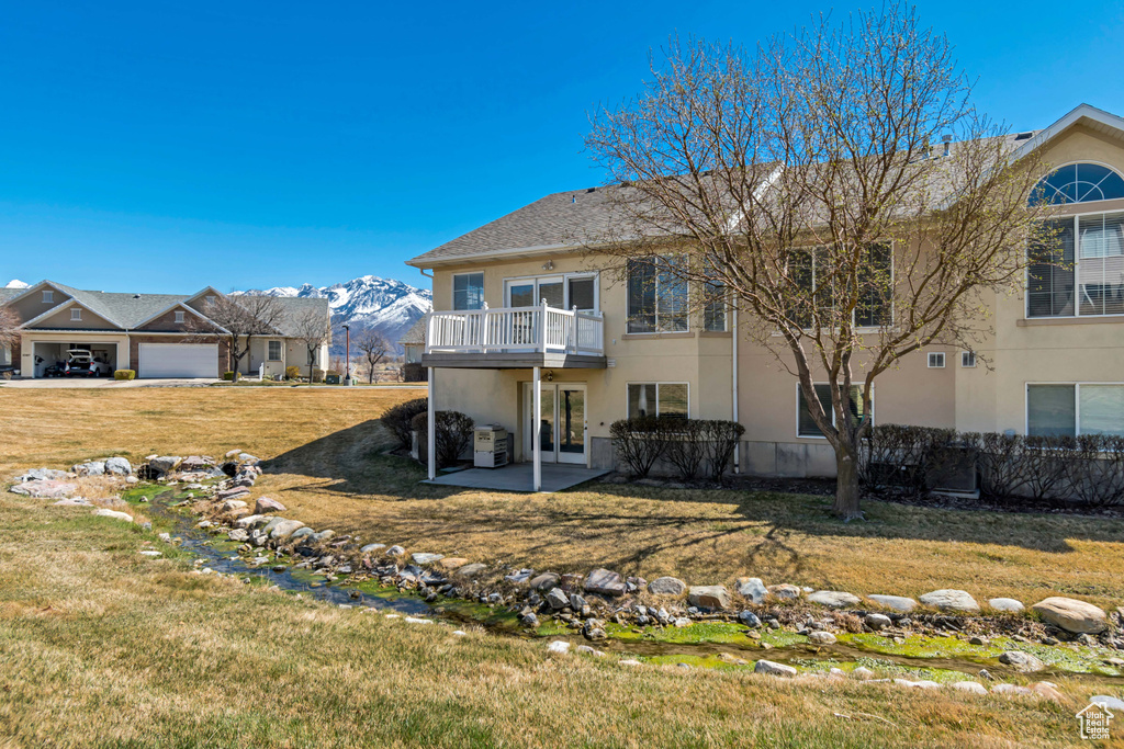 Back of house with a balcony, a lawn, stucco siding, and a mountain view