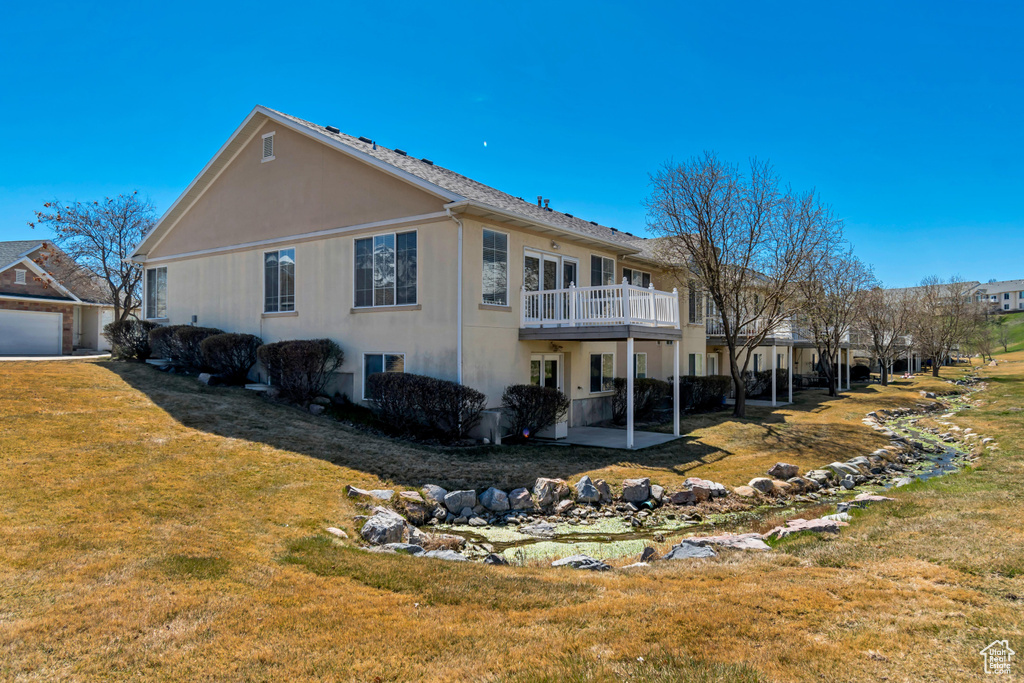 Rear view of house with a lawn, stucco siding, a wooden deck, and a patio