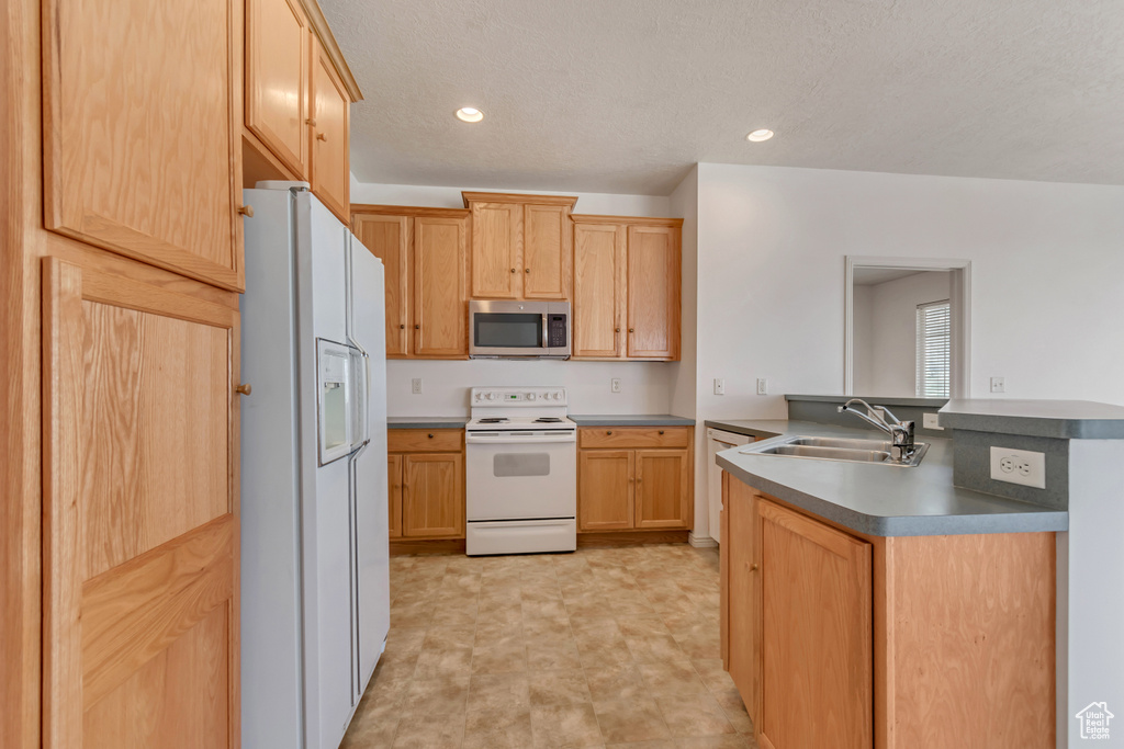 Kitchen featuring a sink, a peninsula, light brown cabinetry, and white appliances