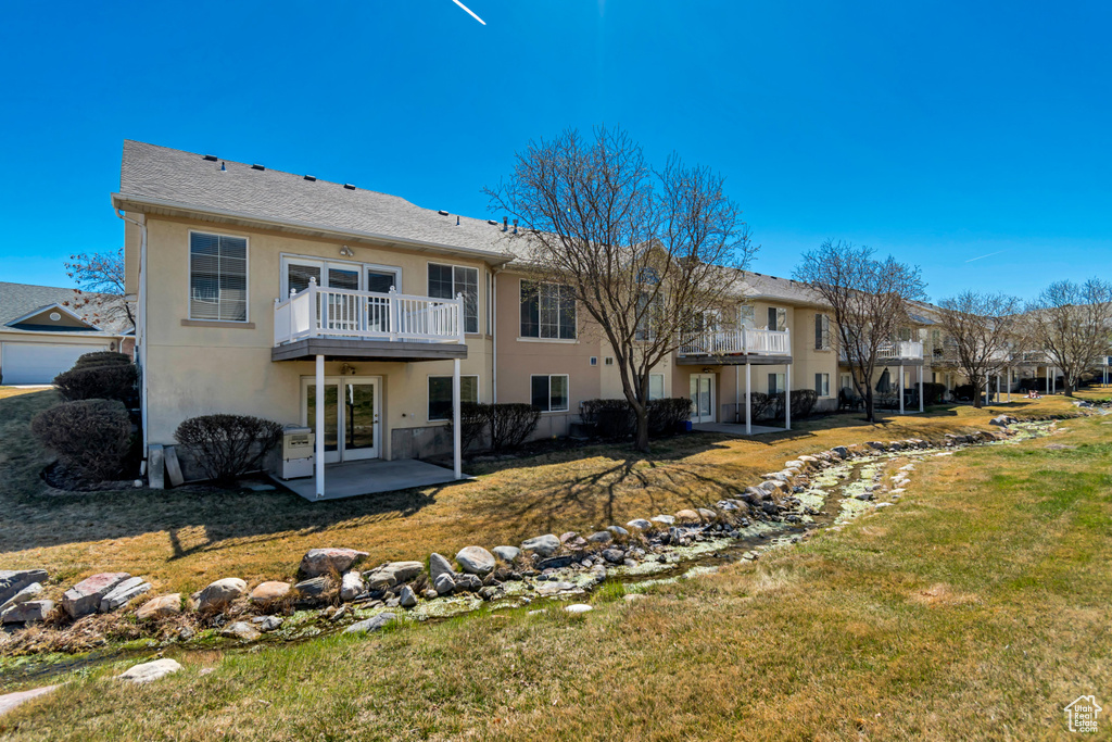 Back of house featuring stucco siding, a lawn, french doors, and a balcony