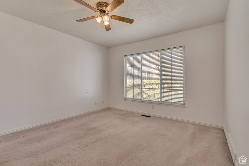 Spare room featuring a textured ceiling, baseboards, light colored carpet, visible vents, and ceiling fan