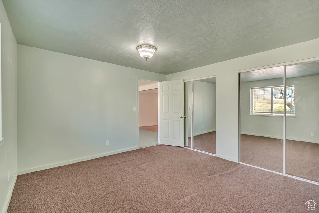 Unfurnished bedroom featuring two closets, carpet flooring, baseboards, and a textured ceiling