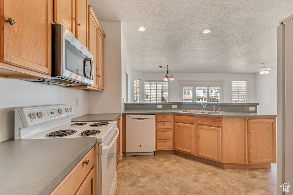 Kitchen featuring white appliances, a textured ceiling, a sink, ceiling fan, and a peninsula