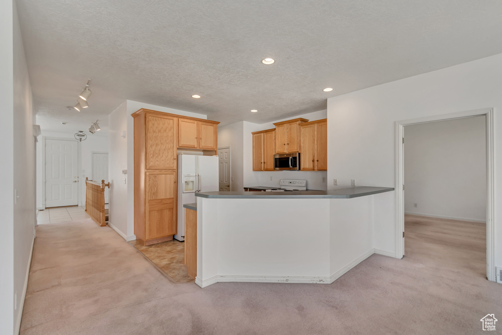 Kitchen with light colored carpet, a peninsula, a textured ceiling, white appliances, and recessed lighting