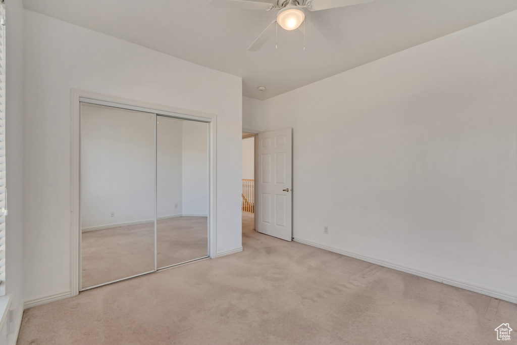 Unfurnished bedroom featuring light carpet, baseboards, a closet, and ceiling fan