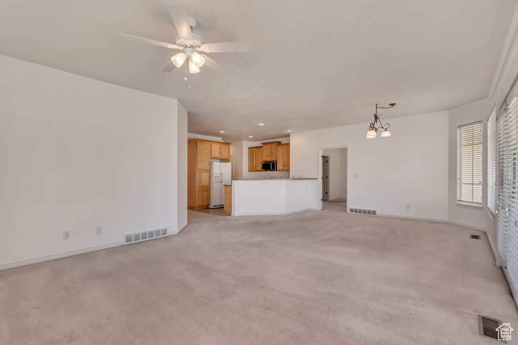 Unfurnished living room with visible vents, ceiling fan with notable chandelier, and light colored carpet