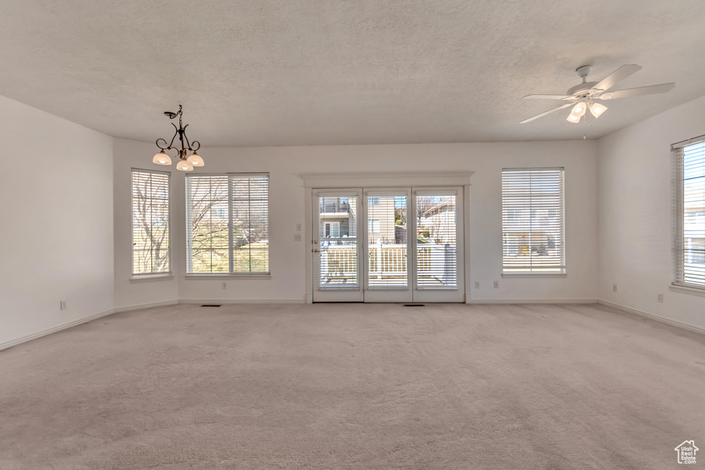 Unfurnished room featuring ceiling fan with notable chandelier, baseboards, light colored carpet, and a textured ceiling