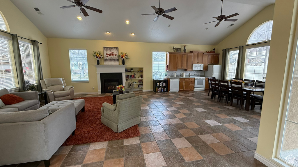 Living room featuring high vaulted ceiling, a ceiling fan, a fireplace, baseboards, and visible vents