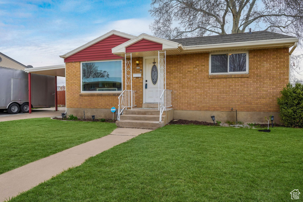 View of front of property featuring brick siding, an attached carport, and a front lawn