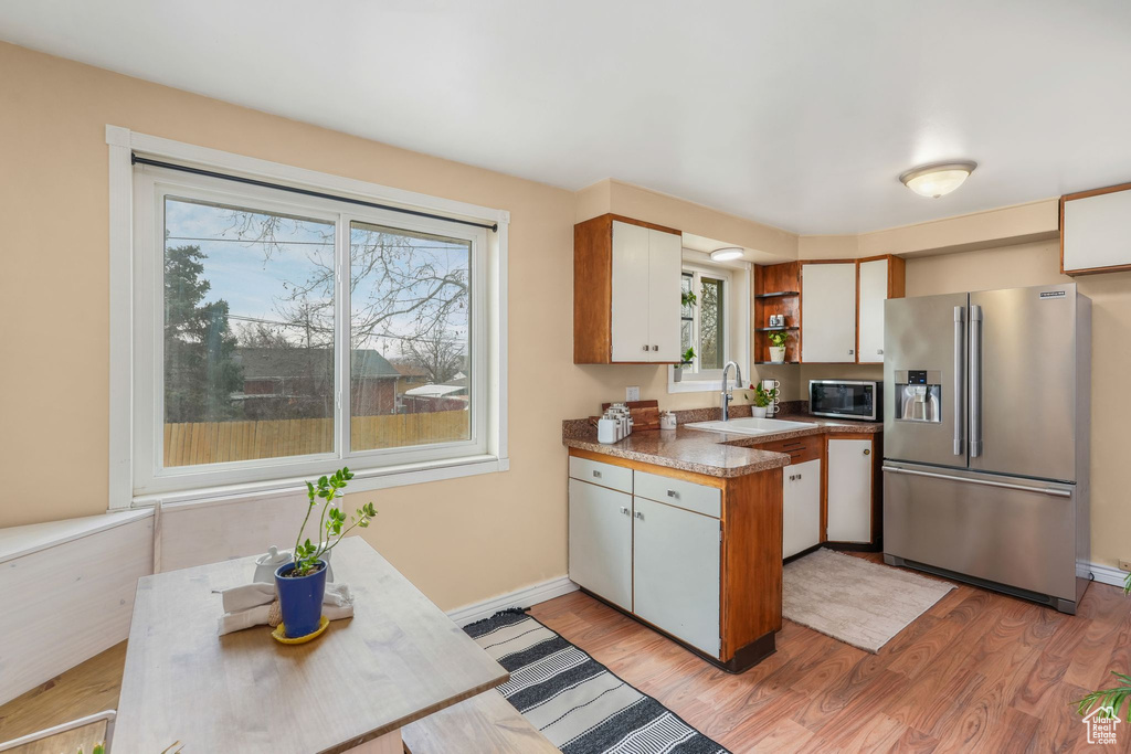 Kitchen with stainless steel fridge, baseboards, a sink, open shelves, and light wood-style floors