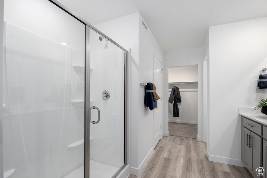 Full bath featuring wood finished floors, a stall shower, a walk in closet, and vanity
