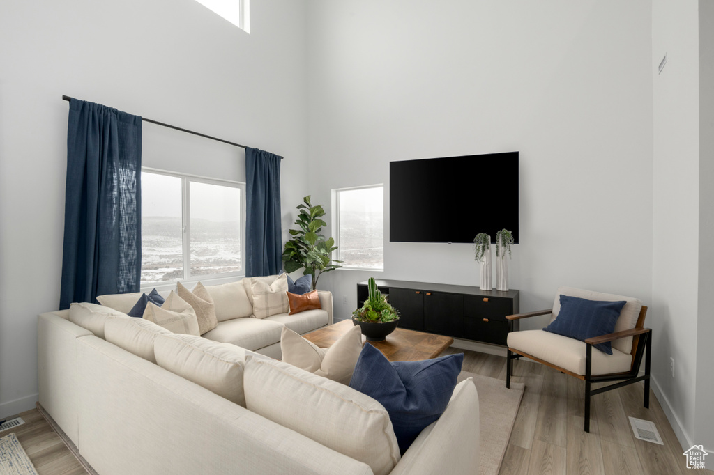 Living room featuring baseboards, a towering ceiling, visible vents, and light wood-type flooring