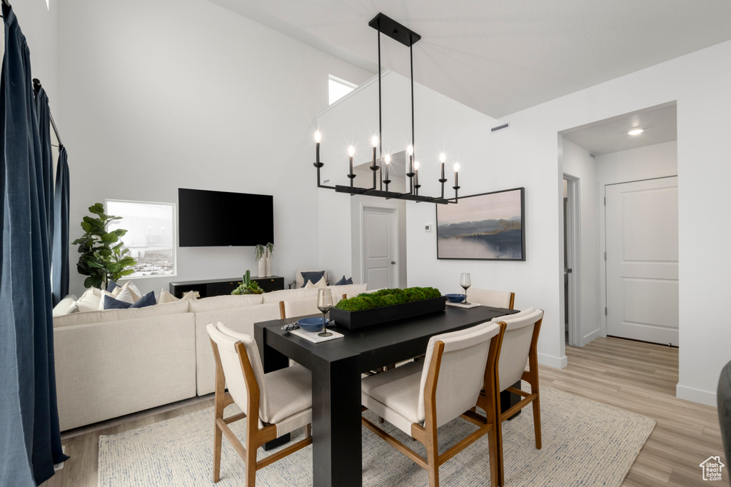 Dining area featuring baseboards, high vaulted ceiling, an inviting chandelier, and light wood-type flooring