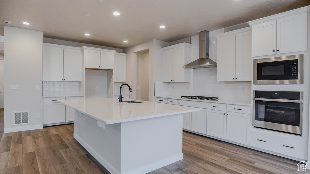 Kitchen featuring a sink, appliances with stainless steel finishes, light wood-type flooring, wall chimney range hood, and visible vents