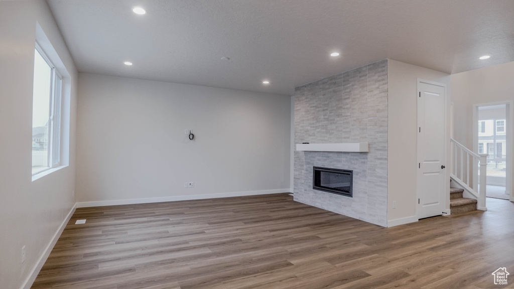 Unfurnished living room featuring recessed lighting, a stone fireplace, stairway, and wood finished floors