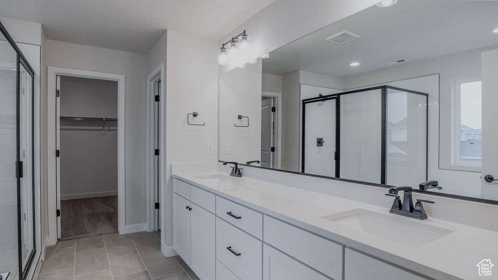 Full bath with a stall shower, double vanity, a spacious closet, and a sink