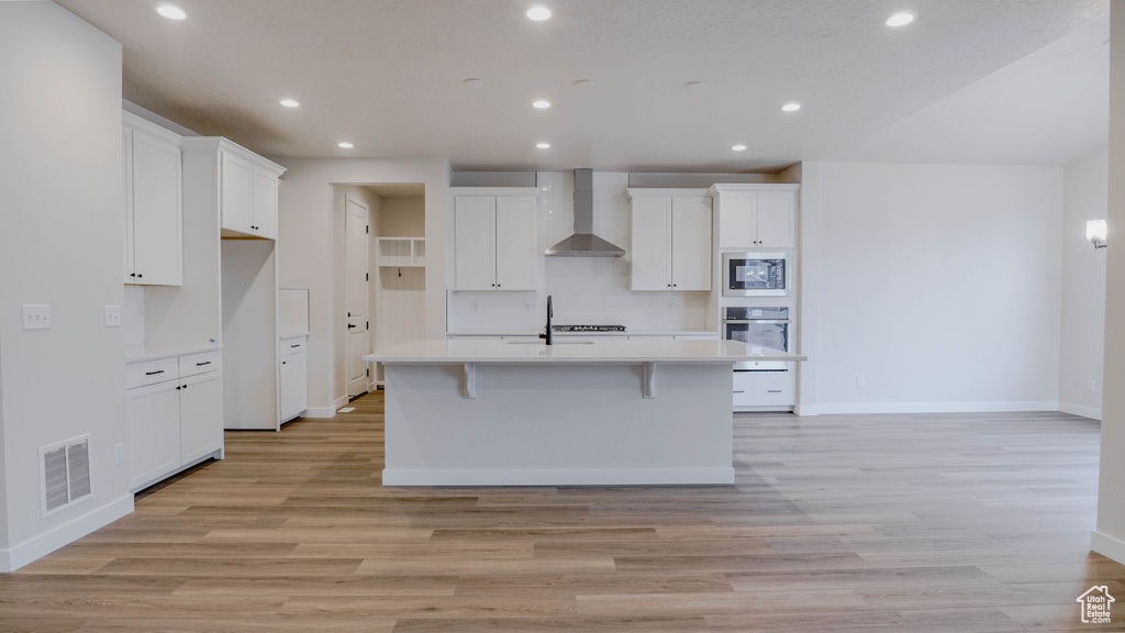 Kitchen featuring light countertops, stainless steel oven, built in microwave, visible vents, and wall chimney range hood