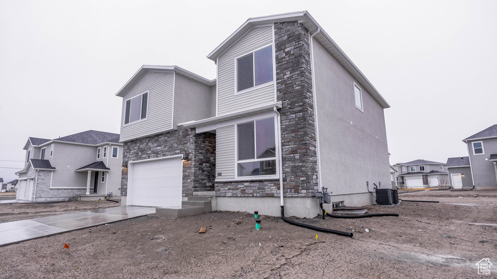 View of front facade with central air condition unit, driveway, an attached garage, and stone siding