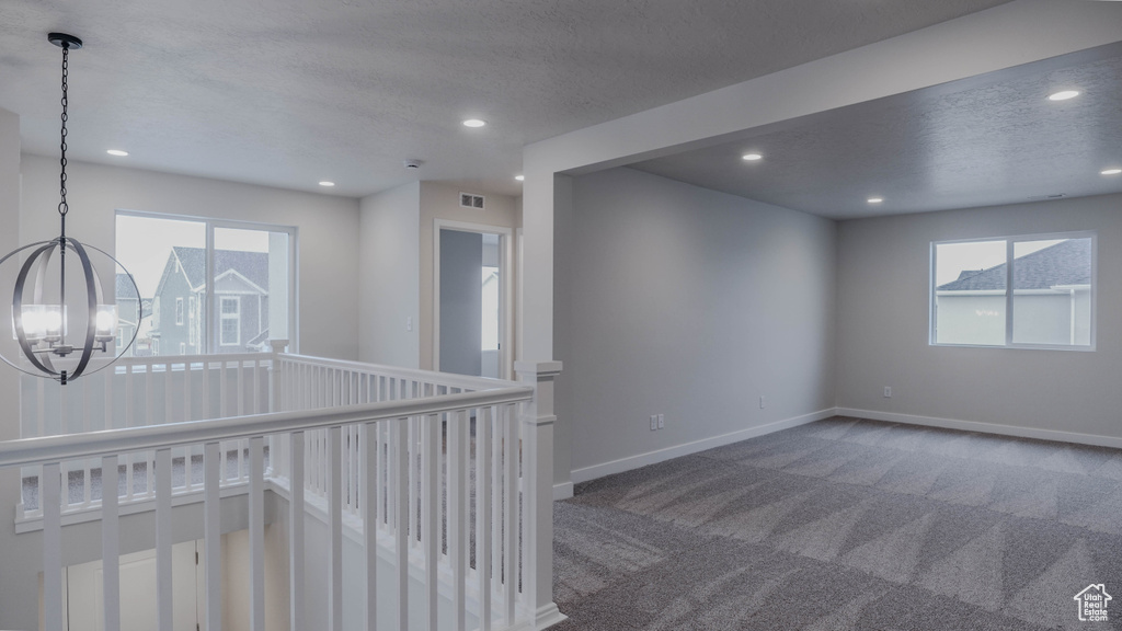 Carpeted empty room featuring baseboards, a textured ceiling, recessed lighting, and a chandelier
