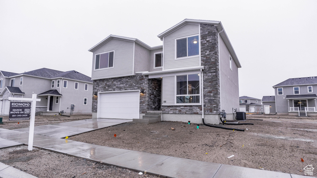 View of front of home featuring stone siding, driveway, cooling unit, and an attached garage
