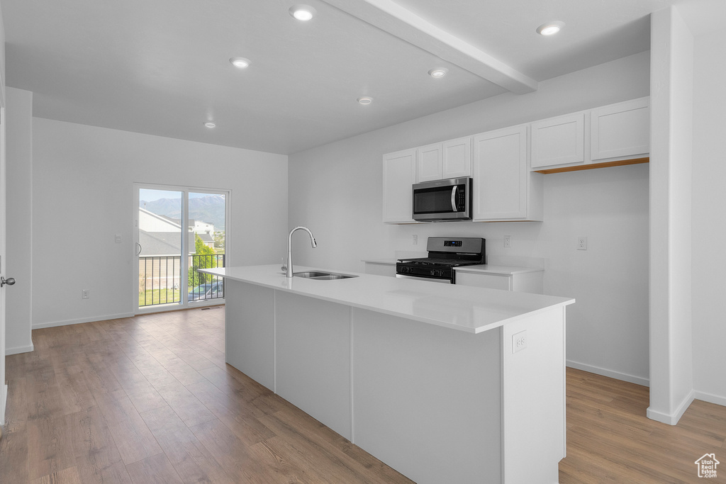 Kitchen with stainless steel appliances, a center island with sink, white cabinetry, a sink, and light wood-type flooring