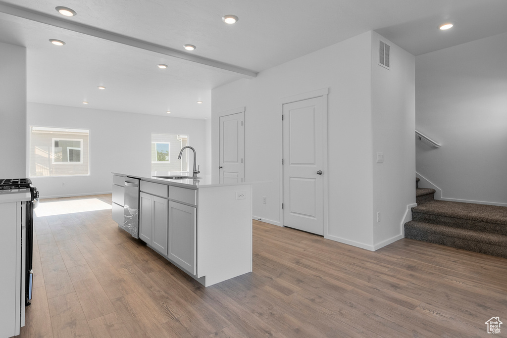 Kitchen featuring stainless steel appliances, baseboards, a sink, light wood-style floors, and beamed ceiling