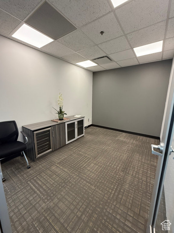 Interior space with baseboards, visible vents, dark carpet, and a drop ceiling