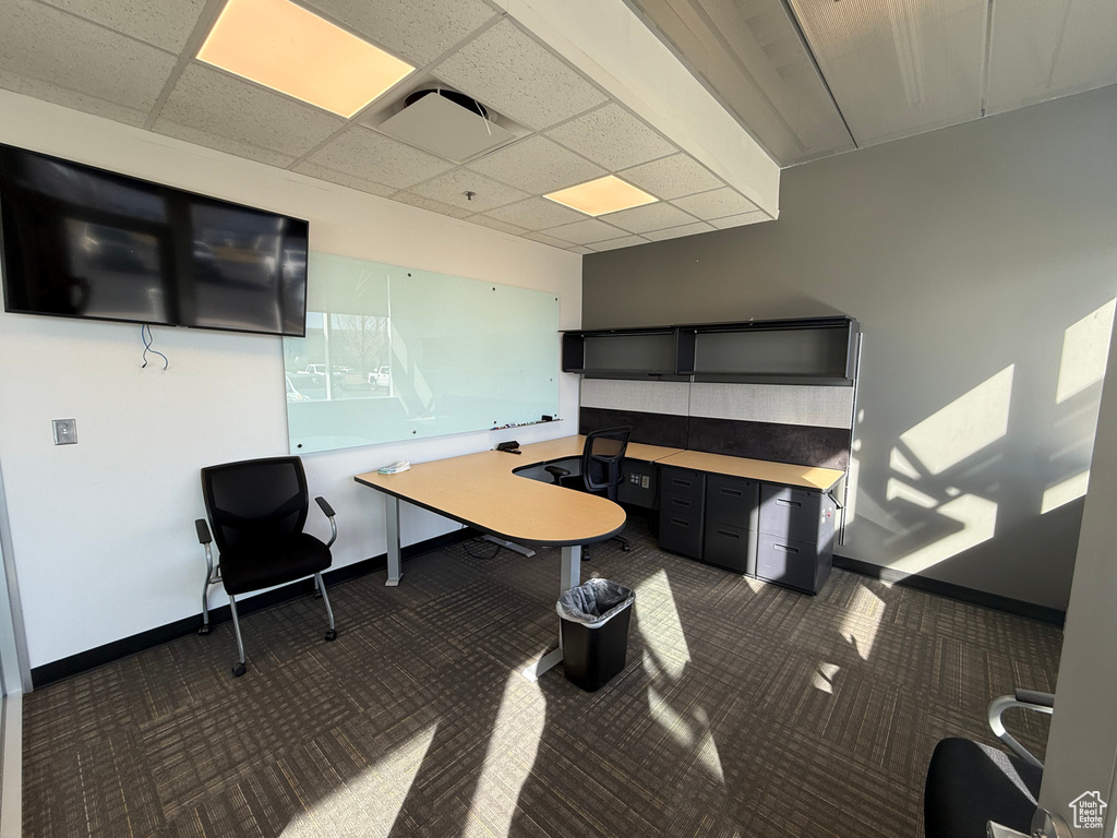 Office space with dark colored carpet, baseboards, and a paneled ceiling
