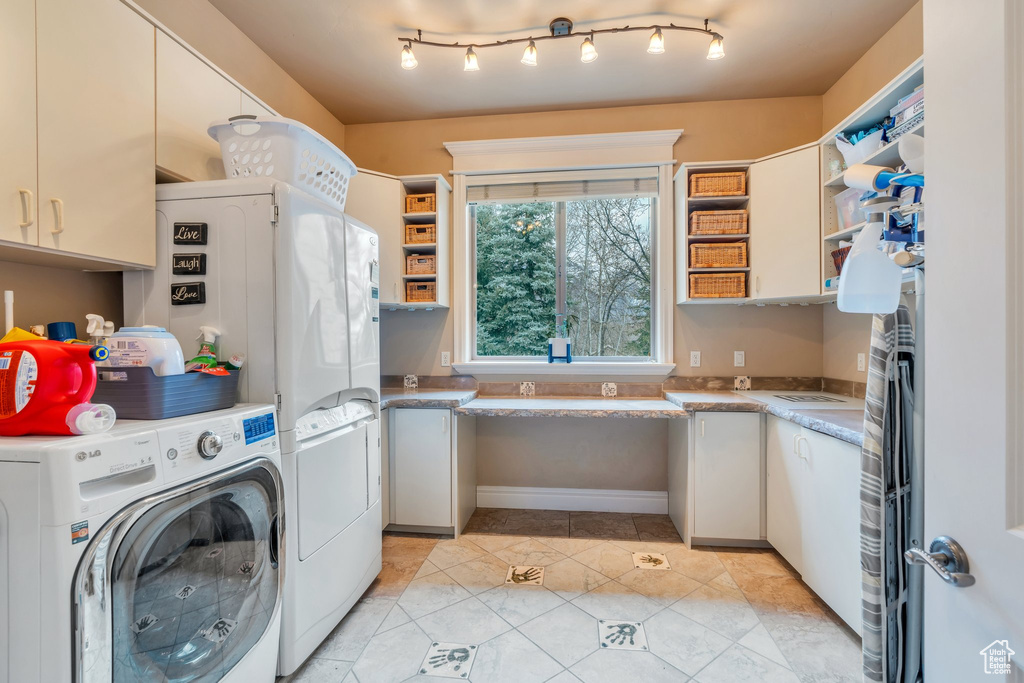 Clothes washing area with light tile patterned floors, cabinet space, and washer and clothes dryer