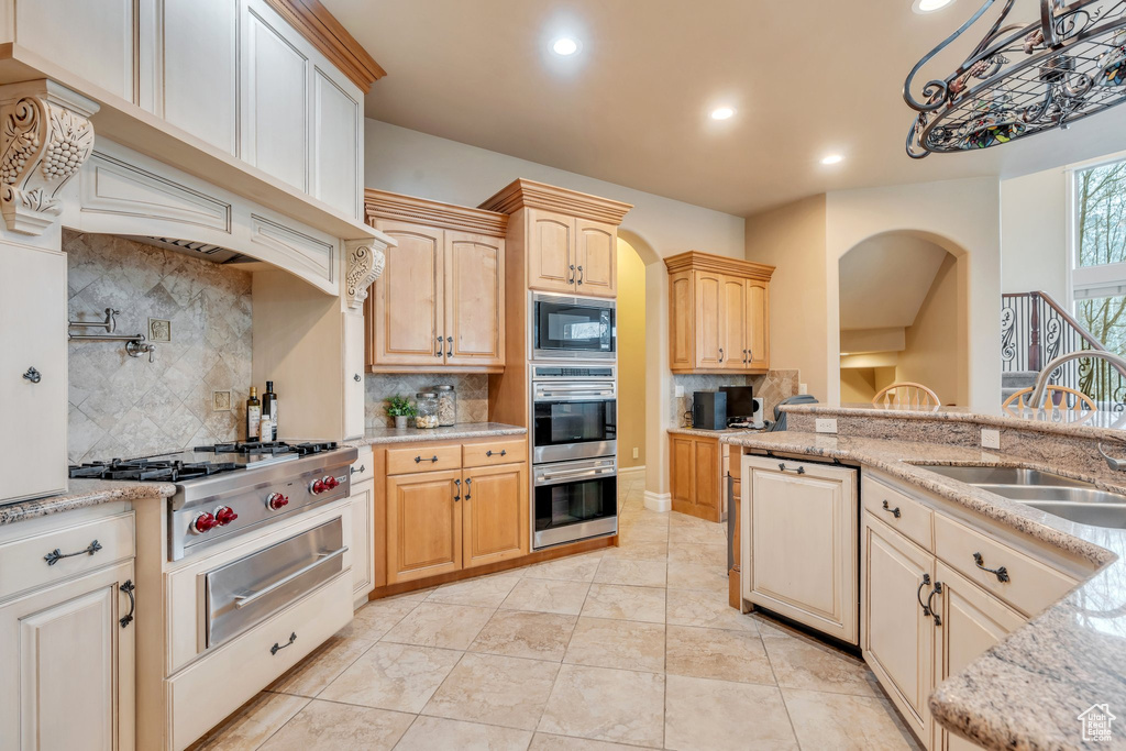 Kitchen with light stone counters, a sink, a warming drawer, appliances with stainless steel finishes, and arched walkways