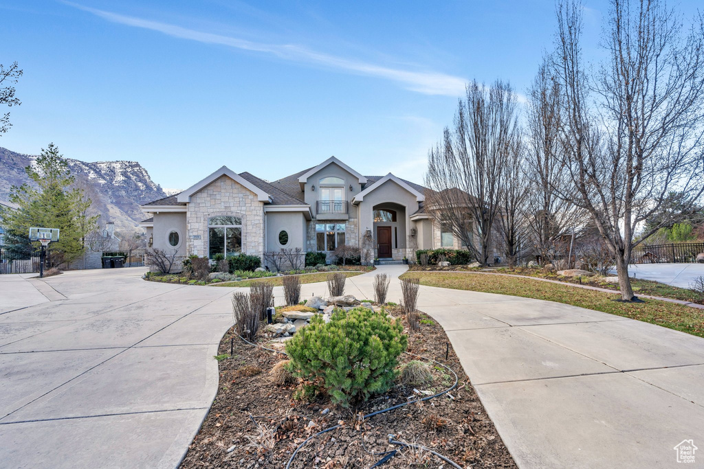 View of front of house with stucco siding, stone siding, a mountain view, and curved driveway