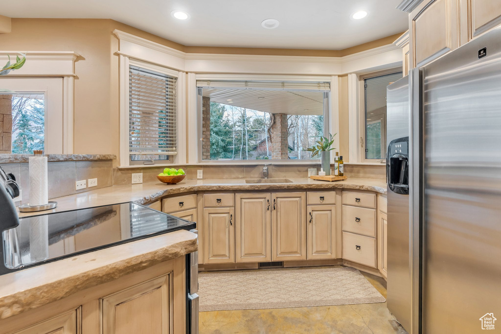 Kitchen with stainless steel fridge with ice dispenser, light brown cabinets, a sink, and light stone counters