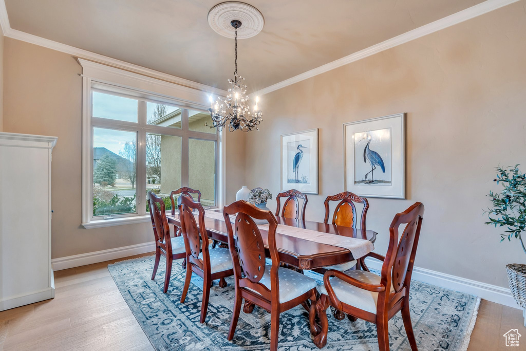 Dining room with baseboards, ornamental molding, light wood-style flooring, and a notable chandelier