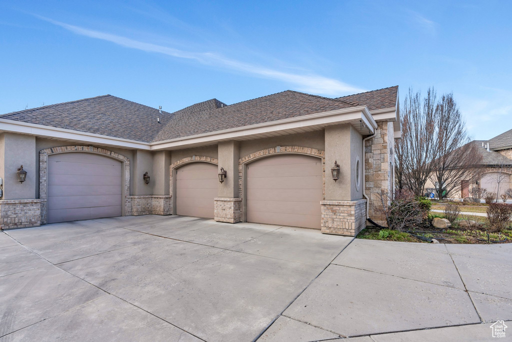 View of front of home with concrete driveway, stucco siding, stone siding, a garage, and a shingled roof