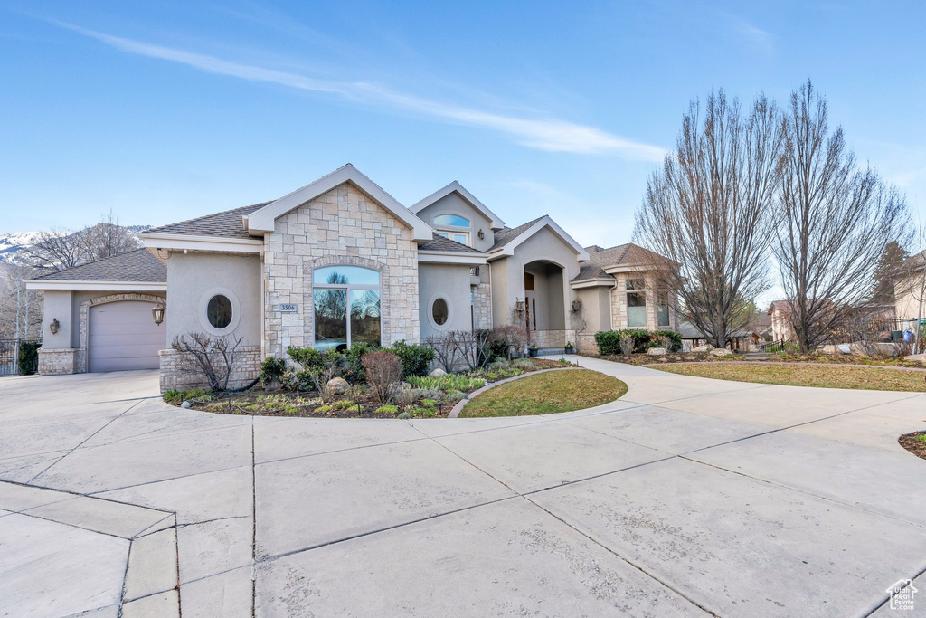French provincial home featuring stucco siding, an attached garage, stone siding, and concrete driveway