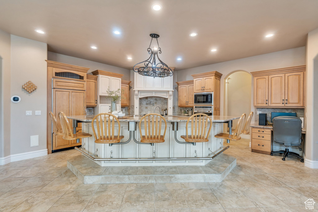 Kitchen with built in appliances, light stone countertops, a kitchen breakfast bar, and tasteful backsplash